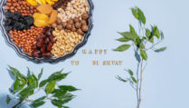 A beautiful festive backdrop with a silver tray with dried fruits and various nuts, traditional treats of Jewish Tu Bi Shvat. green branches. text.