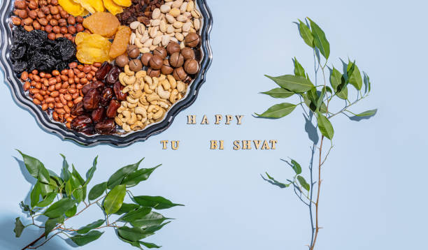 A beautiful festive backdrop with a silver tray with dried fruits and various nuts, traditional treats of Jewish Tu Bi Shvat. green branches. text.